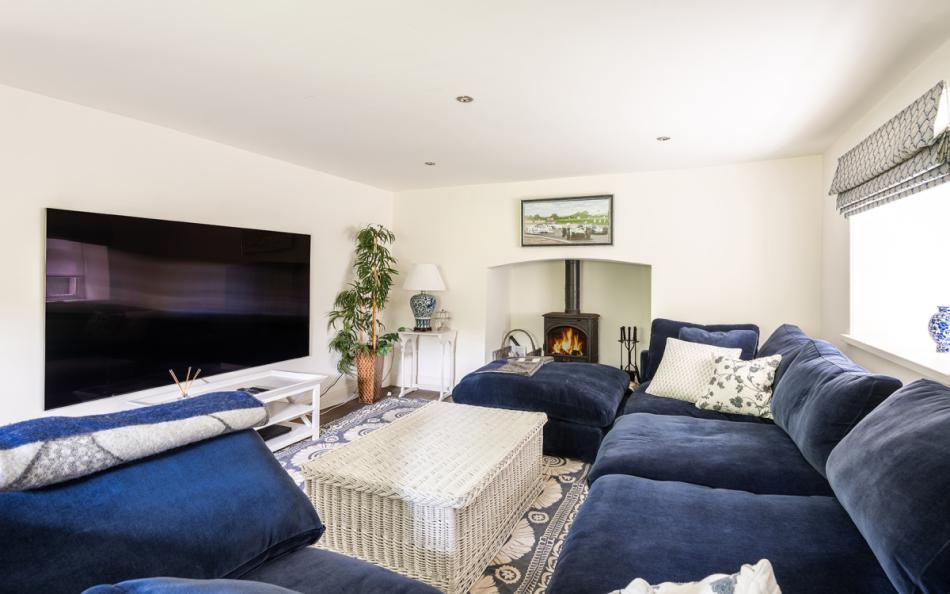 Snug room with large wall-mounted TV and log burner at Bow Bridge House 